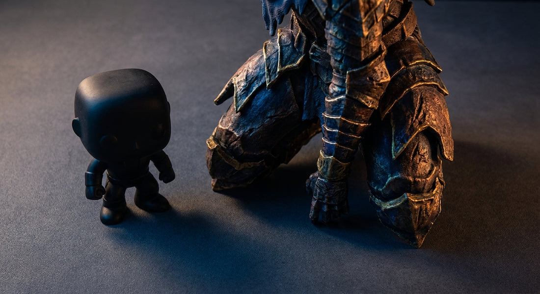 A small vinyl collectible figure sits beside a large, highly detailed 3D printed custom statue under dramatic studio lighting, emphasizing the contrast in scale and craftsmanship.