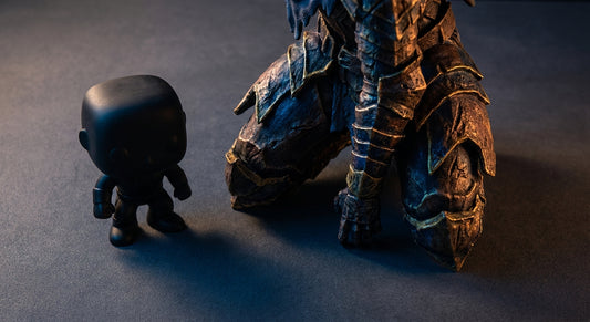 A small vinyl collectible figure sits beside a large, highly detailed 3D printed custom statue under dramatic studio lighting, emphasizing the contrast in scale and craftsmanship.