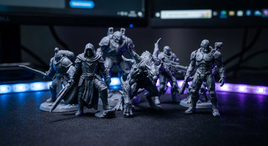A collection of detailed 3D printed gaming character statues displayed on a dark desk under dramatic RGB lighting.