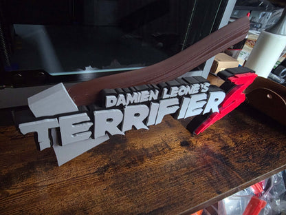 Terrifier 12-inch art piece featuring Art the Clown logo with grey axe motif, horror decor collectible.